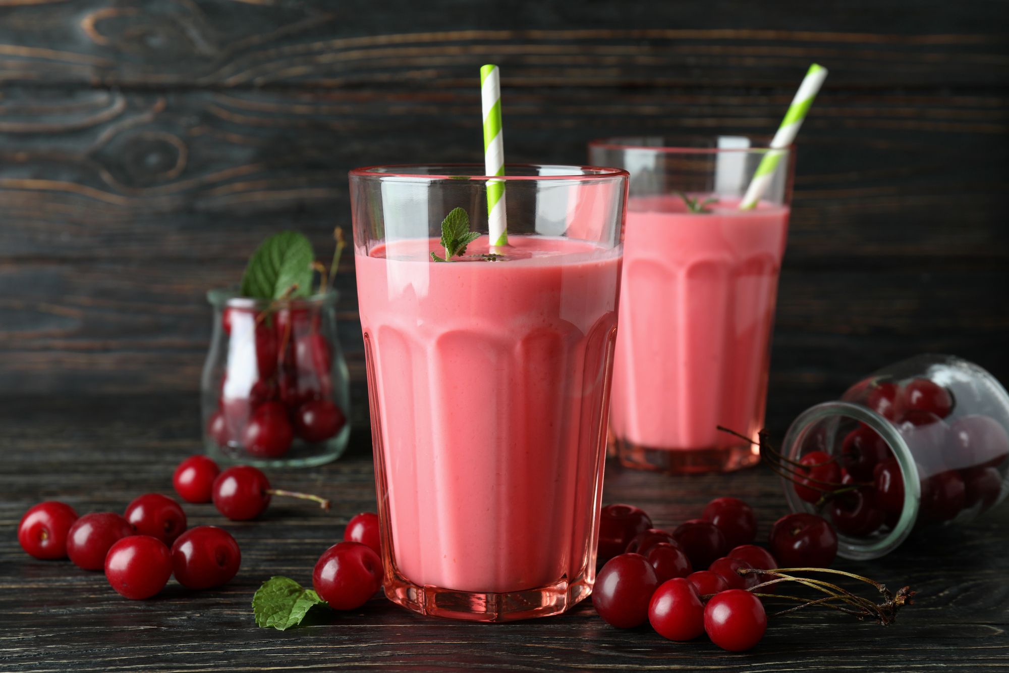 Delicious pink smoothie with mint, straws, and cheries tossed on the side