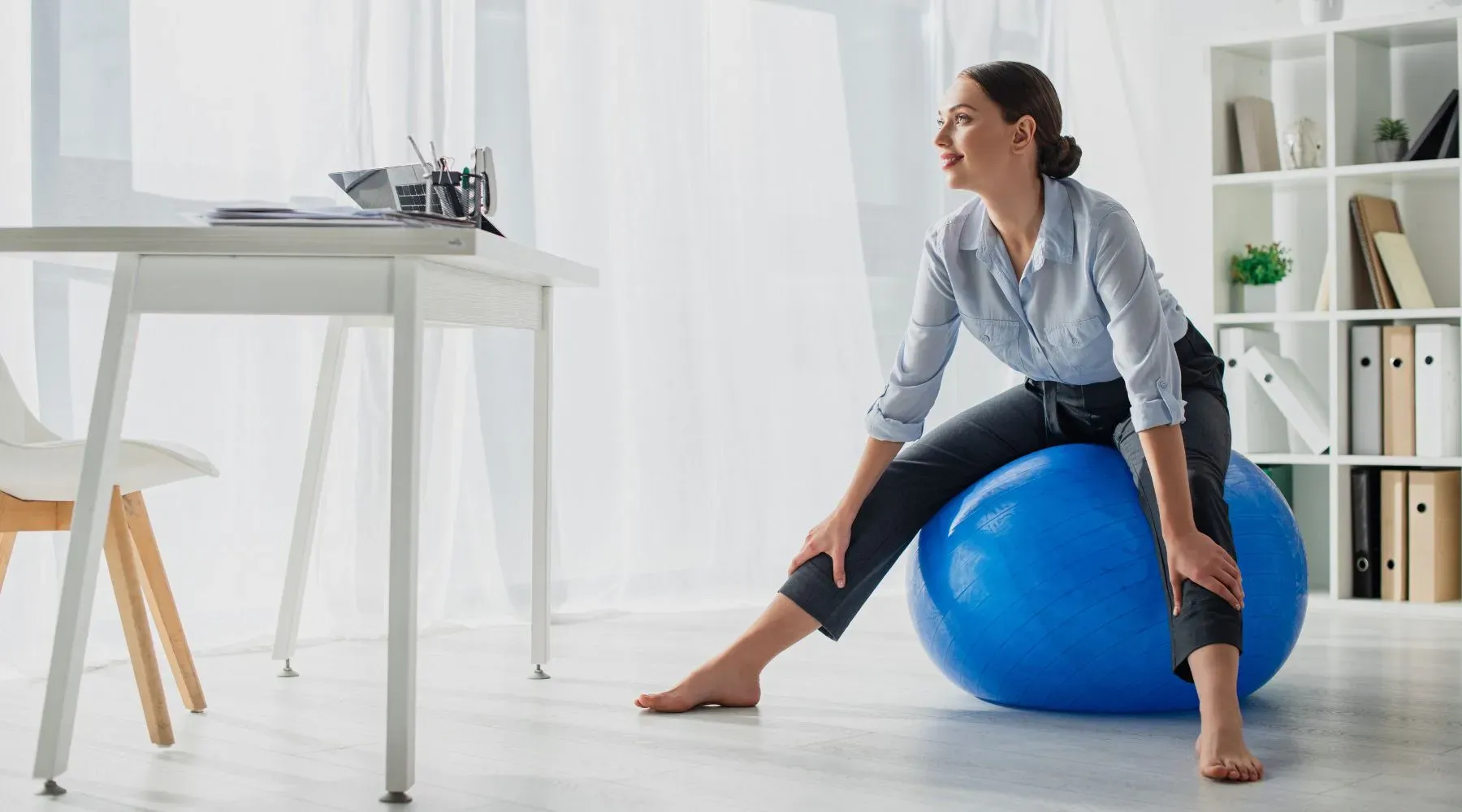 A business woman sitting barefoot on an exercise ball in her office