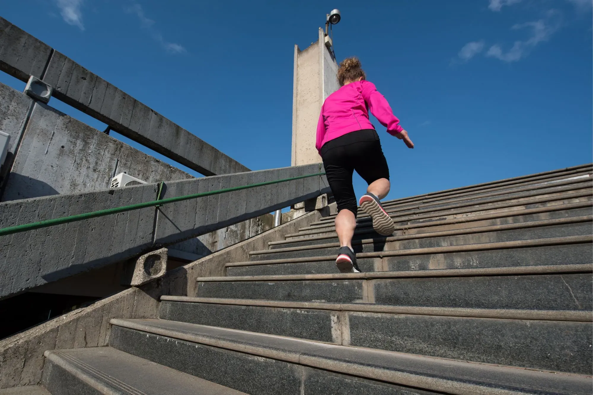 Woman in rose jacket jogging on steps climbing up