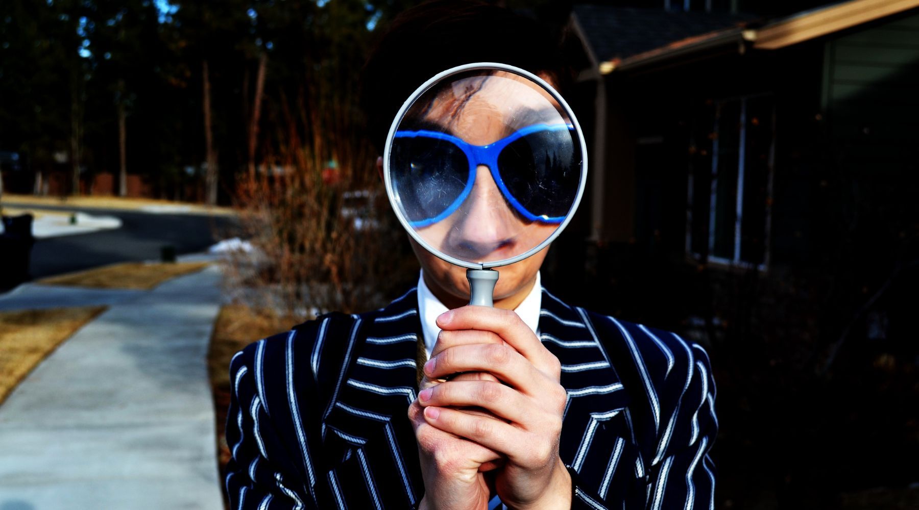 A woman with blue glasses holding a magnifier