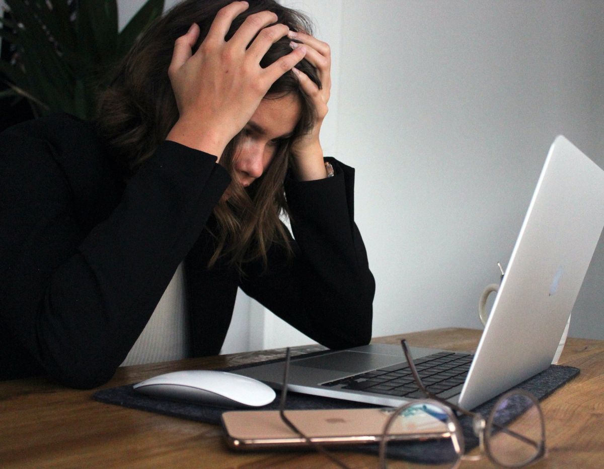 Busy woman holding her head, stressed in front of the laptop