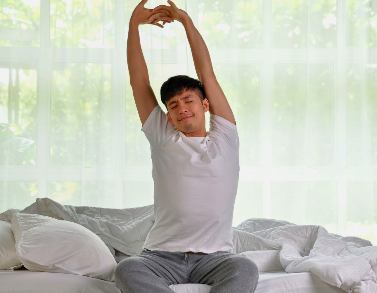 A man waking up stretching with this arms raised and held together