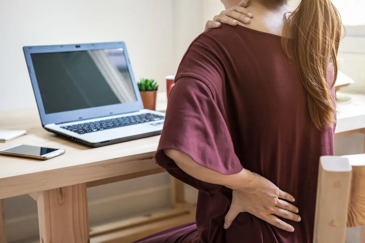 Woman holding her hands on back aching in back pain from sitting
