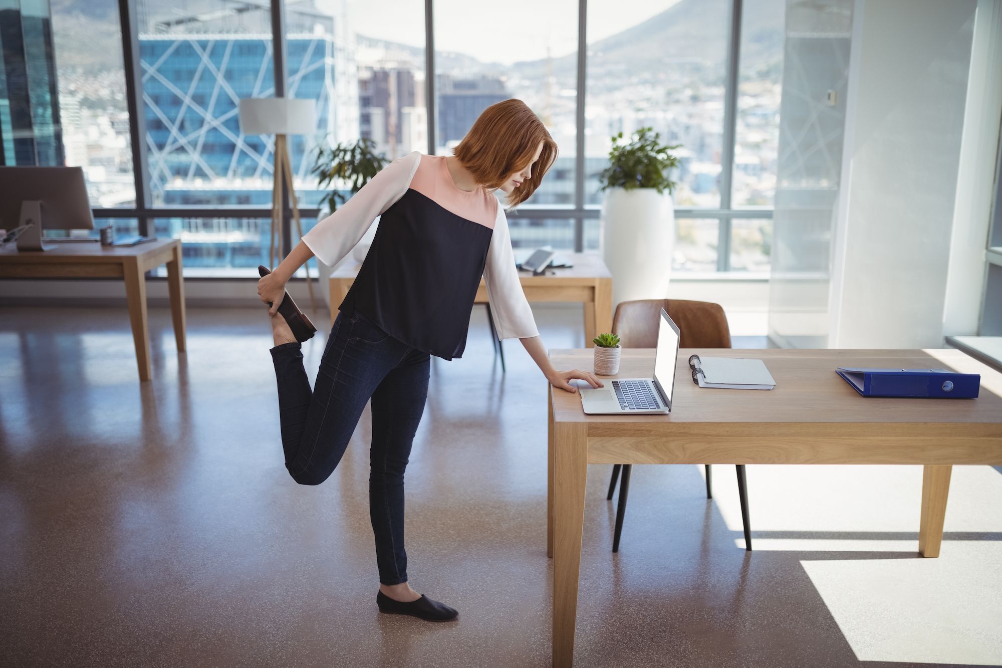 A lady stretching while standing by the laptop in the office