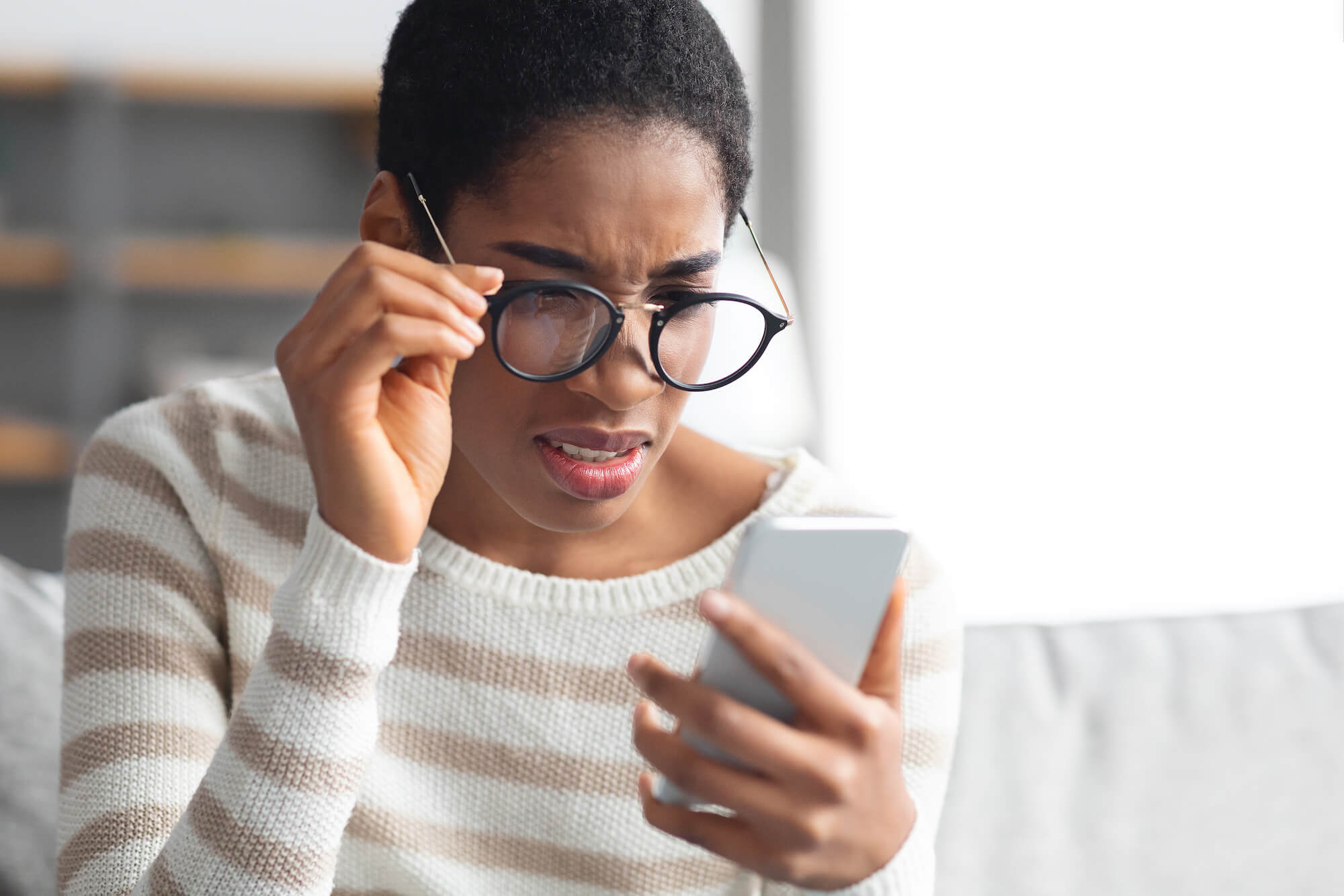 A woman with glasses looking at her phone puzzled